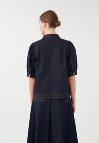 Jeansjacke mit Puffärmeln, dunkelblauem Stoff, kontrastierenden goldenen Nähten und Knopfdetails an den Ärmeln und dem hinteren Saum.