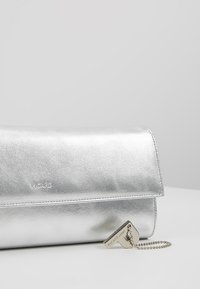 Zilveren metallic handtas met een gladde textuur, een omslagflapontwerp en een bevestigde kettingdetail met een rechthoekige merketiket.