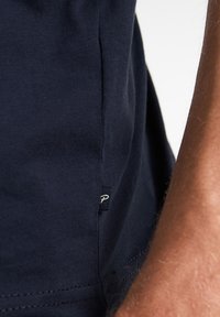 Navy modré bavlněné tričko s detailním pohledem na boční šev a malou etiketu, které ukazuje hladkou texturu a pečlivé šití.