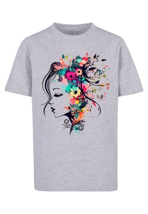 Bambino con t-shirt grigia con stampa floreale colorata sul volto, pantaloni cargo color oliva e scarpe da ginnastica bianche, in piedi con le gambe divaricate.