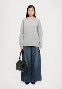 Gray oversized sweatshirt with ribbed hem, paired with wide-leg blue denim jeans. Black handbag details and smooth leather shoes complete the look.