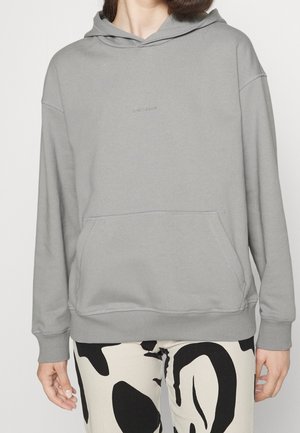 Helle graue Kapuzenjacke aus Baumwollmischgewebe, mit einer Fronttasche, gerippten Bündchen und einer Kapuze mit Kordelzug. Minimalistisches Logo auf der Brust.