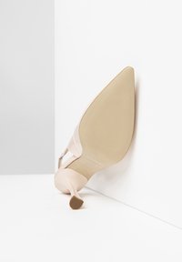 Scarpa con tacco alto di un rosa pallido, dalla punta affusolata e suola testurizzata. Presenta un cinturino sottile e una finitura liscia. La vista angolata mostra l'altezza del tacco.