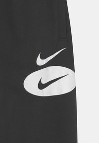 Black sweatpants with a smooth texture, featuring large white Nike swoosh logos on the thigh and hip area.