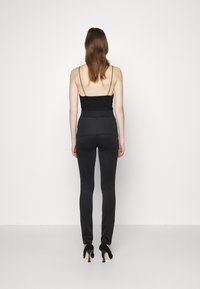 Black fitted pants with a high waistband, smooth texture, and skinny leg design, paired with a black sleeveless top featuring thin straps.
