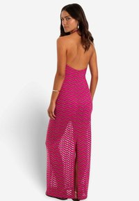 Fuchsia maxi-jurk met chevronpatroon, open rug en een split aan de zijkant. Materiaal lijkt glanzend, aansluitend, met een halternek.