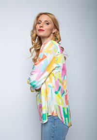 Bunte Bluse mit einer Mischung aus großen, abstrakten Buchstaben in Pink, Gelb, Blau und Grün auf einem hellen Hintergrund; lange Ärmel und lockere Passform.