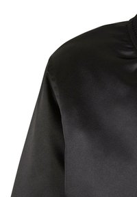 Detailní záběr černé saténové bomber bundy zobrazující rameno, rukáv a žebrovaný límec na bílém pozadí.