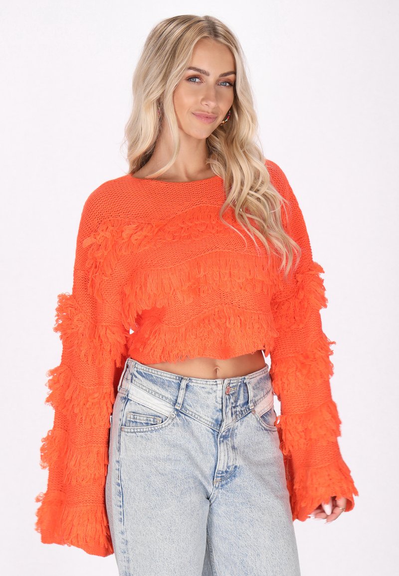 Orangestraßiger Pullover mit strukturiertem Fransen-Detail, weiten Ärmeln und Strickstoff, kombiniert mit hochgeschnittenen blauen Denim-Jeans.