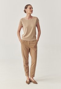 Top beige a maniche corte con bordi bianchi, abbinato a pantaloni beige a gamba affusolata e ballerine marroni a punta. Tessuto liscio, design casual.