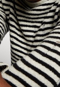 Sweter w czarno-kremowe paski, wykonany z teksturowanego dziania, z szerokim okrągłym dekoltem oraz delikatnym postrzępieniem na dolnym brzegu i rękawach.