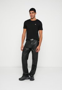 Tricou negru din bumbac cu mâneci scurte și un mic logo; asortat cu pantaloni negri din piele lucioasă, cu mai multe buzunare. Adidași negri.