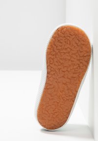 Sneaker bianco con suola in gomma arancione, testurizzata e flessibile. Presenta un bordo superiore testurizzato con sottili righe. Design pulito e minimalista.