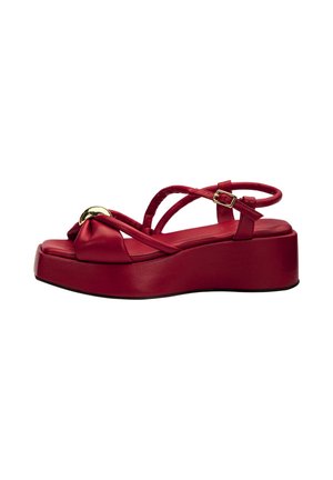 Red platform sandal with a cushioned sole, crossover straps, ankle buckle, and decorative gold-tone accent on the front strap.