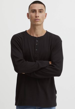 Svart langermet henley skjorte i ribbestrikket tekstur, med rund hals og fire-knappers plissering. Slim fit med detalj av sidelapp.