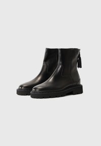 Bottines en cuir noir avec une finition mate, bout arrondi, semelle en caoutchouc noir épaisse et fermeture éclair sur le côté avec un détail de gland.