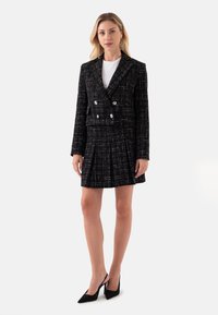 Zwart-wit geruite op maat gemaakte blazer met dubbele knopen, gecombineerd met een geplooide rok; inclusief een witte top en zwarte puntige hakken.