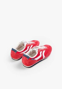 Zapatillas de ante rojas con rayas blancas, cordones blancos y un acento en el talón azul marino. Presentan un acabado texturizado y una suela de goma de perfil bajo.