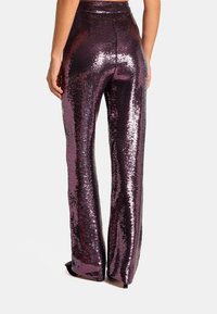Spodnie z wysokim stanem w błyszczące fioletowe cekiny, o gładkiej fakturze i dopasowanej sylwetce, która podkreśla nogi.