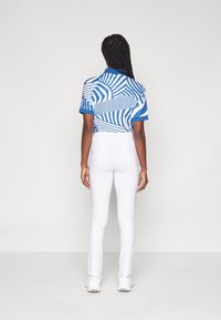 Short-sleeve polo with a blue and white abstract pattern, paired with fitted white pants and white sneakers. Smooth fabric, modern fit.