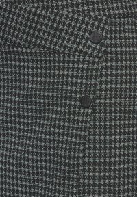 Un tessuto a fantasia nero e blu chiaro presenta un design a houndstooth testurizzato, con due bottoni neri vicino alla vita.