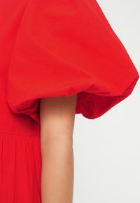 Κόκκινο φόρεμα με φουσκωτά μανίκια από ελαφρύ ύφασμα με ρυτιδωτή υφή και ρομαντική σιλουέτα. Διαθέτει σφιχτή μέση και φούστα με στρώσεις.