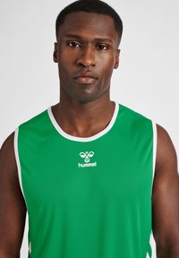 Top sportivo verde realizzato in materiale leggero, con rifiniture bianche attorno al colletto e alle braccia, e un logo sul davanti.
