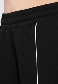 Sorte sweatpants lavet af blødt bomuldsblanding, med en ribbet talje og en hvid accentstribe langs siden.