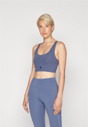 Blauwe sportbh met een aansluitend ontwerp, brede bandjes en een cropped lengte. Heeft een subtiel logo en contrasterende stiksels. Gecombineerd met bijpassende leggings.