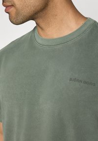 Green cotton t-shirt with a crew neck, featuring a subtle texture and a printed logo "BJÖRN BORG" in black on the chest.
