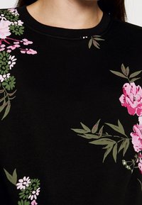 Tejido negro con patrones florales en rosa y blanco y hojas verdes, mostrando un escote redondeado en la parte superior del pecho y el cuello de una persona.