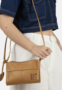 Tan læder crossbody taske med lynlåslukning, præget logo og justerbar skulderrem. Designet har en minimalistisk rektangulær form.