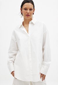 White, oversized button-up shirt made of smooth fabric, featuring a classic collar and long sleeves with wide cuffs.