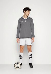 Camiseta deportiva gris de manga larga con cremallera de cuarto, pantalones cortos blancos, tacos de fútbol negros y calcetines a rayas blancos y negros. Balón de fútbol en blanco y negro.