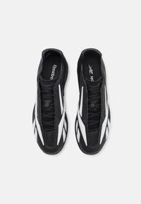 Scarpe da ginnastica nere con accenti bianchi, caratterizzate da un design testurizzato, colletto imbottito e lacci, che mostrano una forma affusolata.