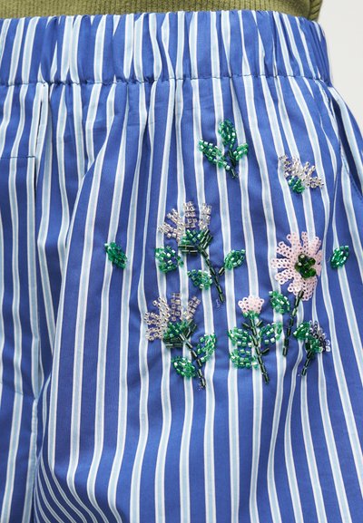 Tissu à rayures verticales bleu et blanc avec broderie florale perlée verte et rose près d'une ceinture élastique.