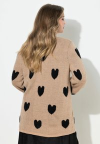 Cardigan beige lavorato a maglia con motivi a cuore neri, taglio ampio, maniche lunghe, polsini e orlo a costine. Tessuto morbido. Vista posteriore mostrata.