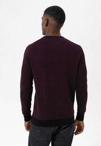 Pull en tricot violet foncé avec un col rond, des poignets et un ourlet côtelés. Présente une texture lisse et une coupe ajustée, porté avec un jean foncé.