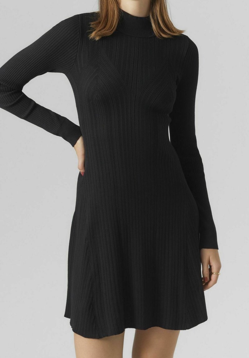 Robe tricotée noire à côtes avec manches longues, col montant, jupe évasée et lignes diagonales texturées. Détails comprenant des poches latérales.