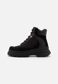 Botas altas pretas com uma mistura de pele lisa e texturas de camurça. Sola grossa e resistente com um padrão de solado proeminente e detalhes de ilhós.