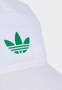 Witte pet van stof met een textuur van het groene Adidas trefoil logo en drie groene strepen, met zichtbare stikdetails.