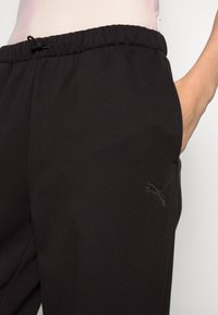 Czarne spodnie dresowe wykonane z miękkiego materiału, z elastycznym pasem ze sznurkiem, bocznymi kieszeniami i małym haftowanym logo.