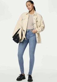 Casaco de ganga oversized em bege claro, blusa às riscas, jeans skinny azul claro e sapatos de plataforma pretos. Modelo a segurar uma bolsa preta.