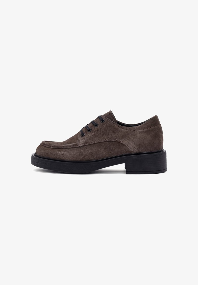 Brown suede lace-up shoe with a rounded toe and black rubber sole. Features five eyelets and a textured finish. Minimalist design.