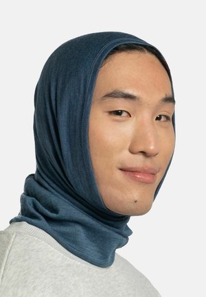 Man met een blauwe rekbare kap die hoofd en nek bedekt, licht glimlachend, tegen een effen lichte achtergrond.