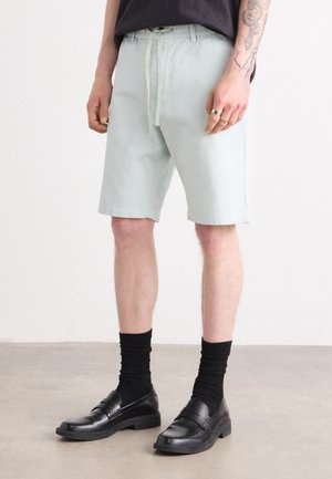 Lyse grønne shorts med en afslappet pasform, snøre i taljen og to sidelommer. Sorte loafers parret med sorte ribbede sokker.