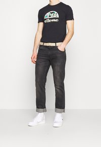 Černé tričko s barevným logem elleese, béžový opasek, tmavé džíny s ohrnutými kotníky a bílé tenisky. Neformální oblečení.