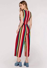 Mono a rayas con líneas verticales en rojo, azul, amarillo y rosa. Diseño sin mangas con un escote alto, combinado con zapatos de plataforma azules.