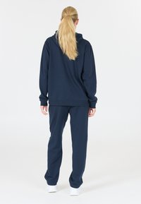 Marinblå hoodie och matchande sweatpants i mjukt tyg, med ribbade ärmslut och midjeband. Minimalistisk design utan synliga mönster.