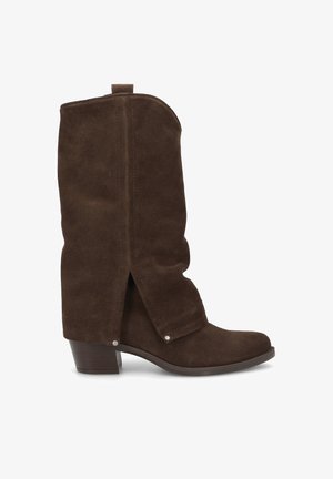 Braune Wildleder-Ankle Boots mit schlabberigem Design, niedrigem Blockabsatz und Druckknopf-Akzenten. Sie verfügen über eine abgerundete Zehenpartie und eine weiche Textur.